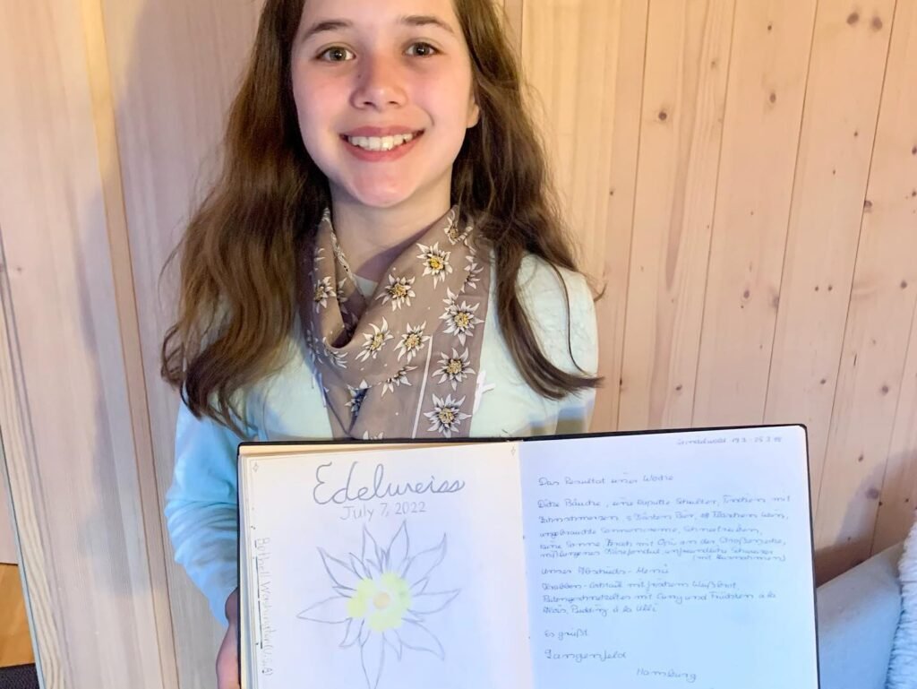A young person smiles while holding a journal titled 'Embracing Solitude' featuring a flower sketch and handwritten text.