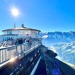 Skyline Walk A scenic overlook at a mountain station offers stunning panoramic views of snow-capped peaks. The bright sun illuminates the clear blue sky.