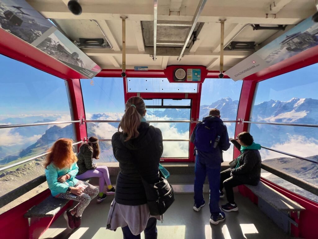 A group of travelers enjoys panoramic views of snow-capped mountains from a cable car.