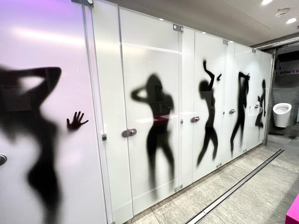 A modern bathroom featuring frosted glass shower doors with shadowy silhouettes of individuals, including one hand pressing against the glass.