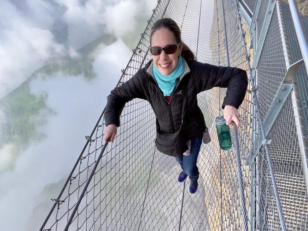 A person walking on a suspension bridge above a sea of clouds in the mountains.