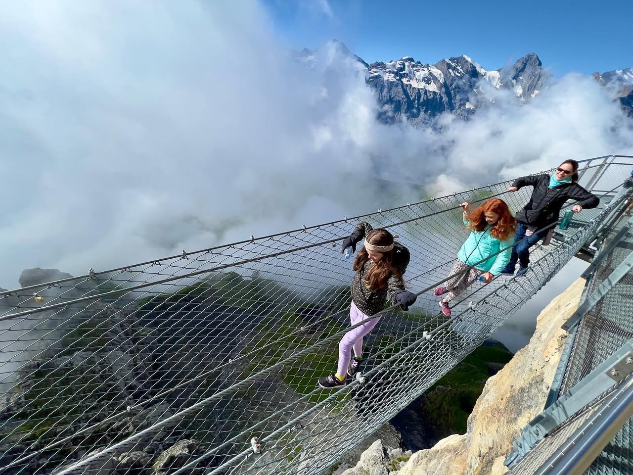 Skyline Walk A group of people carefully crossing a suspended wire mesh bridge over a steep cliff with clouds in the background.