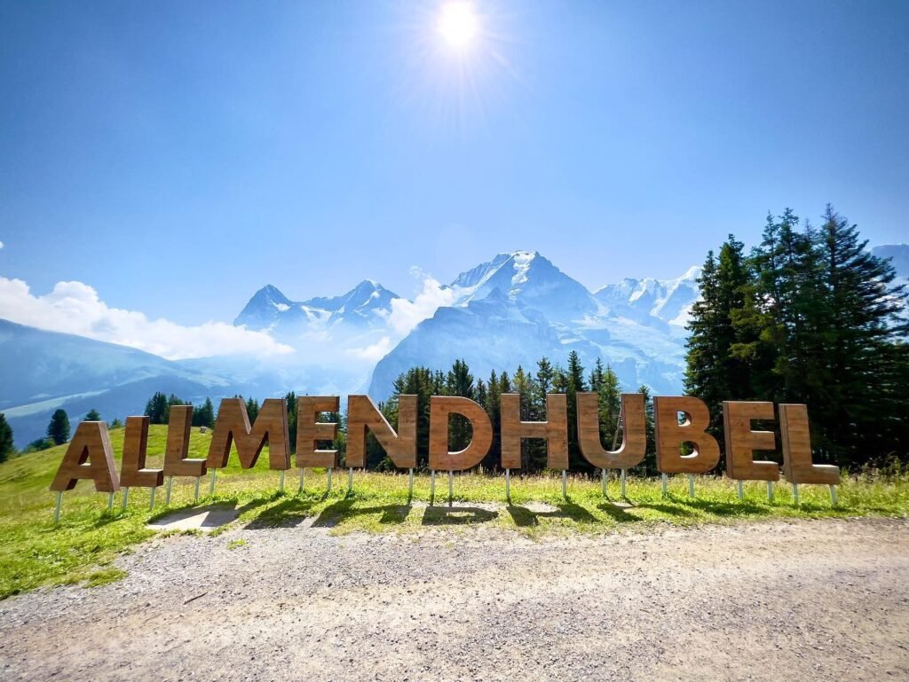 Large wooden letters spelling Almendhübel in front of snowy peaks.