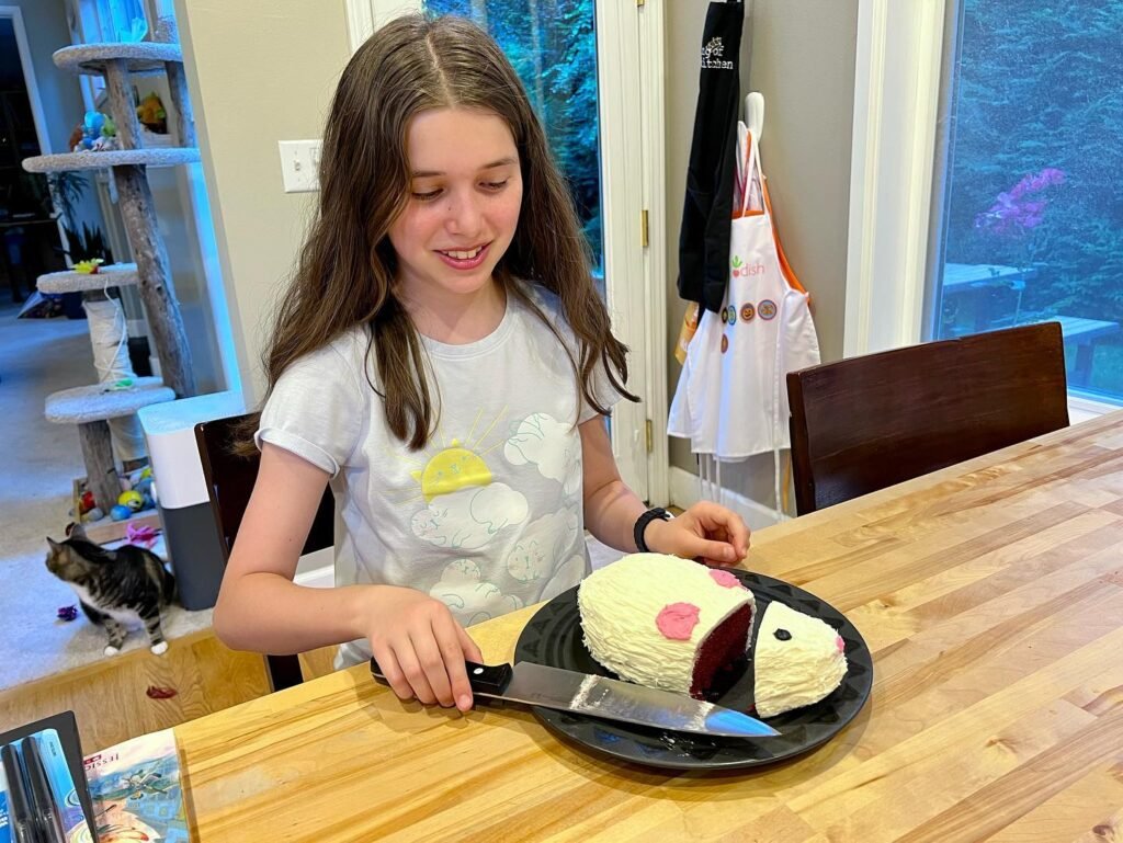 A person cutting a white cake with pink accents on a table.