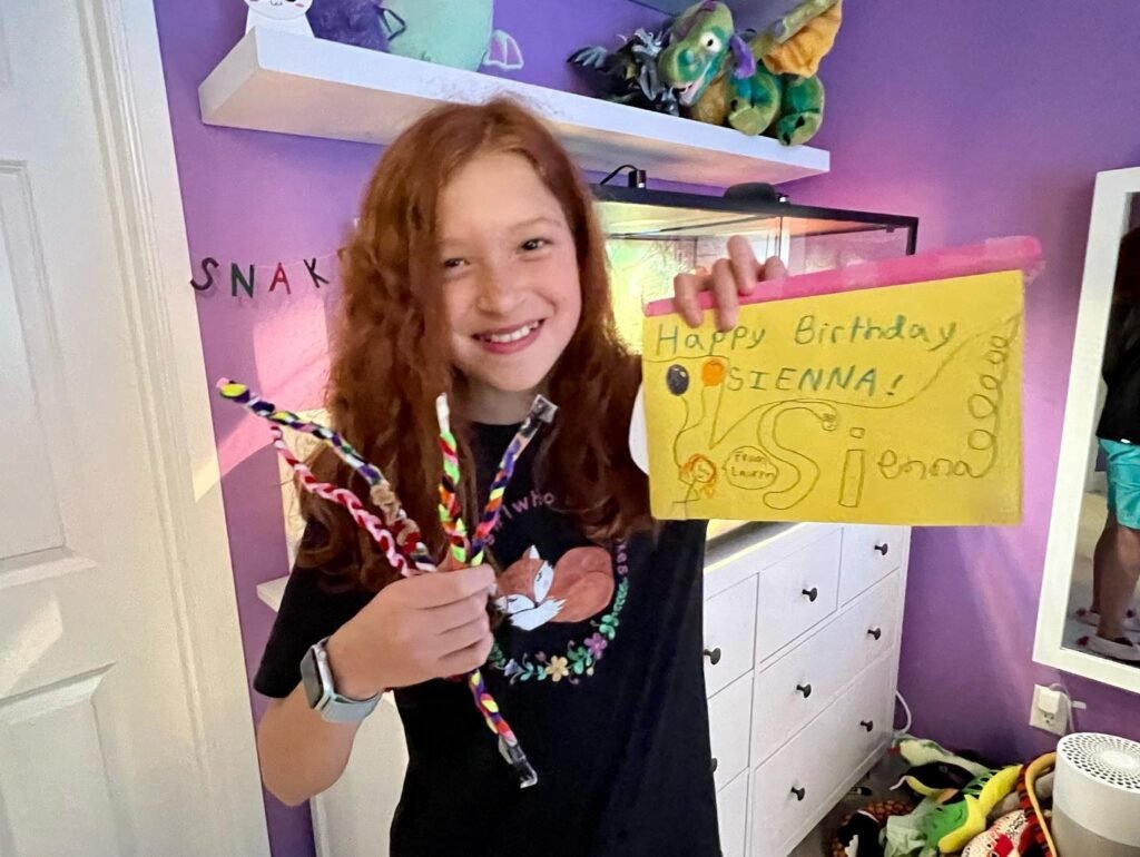 A child holds a handwritten birthday card and party noisemakers in a room with purple walls and white styling.