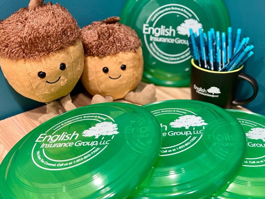 Acorn plush toys and green English Insurance Group frisbees displayed with a black mug of pens on a wooden surface.