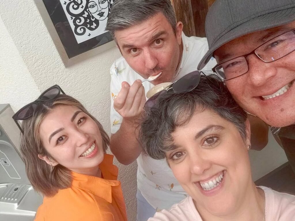 A group of four people smiling and laughing together in a cozy indoor setting while trying some dessert. This photo captures a moment of fun during a sharing family meal.