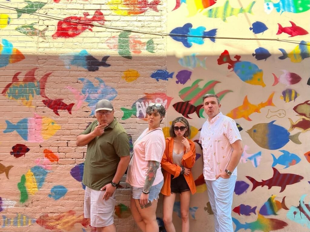A group of individuals posing in front of a vibrant mural featuring many colorful fish silhouettes.