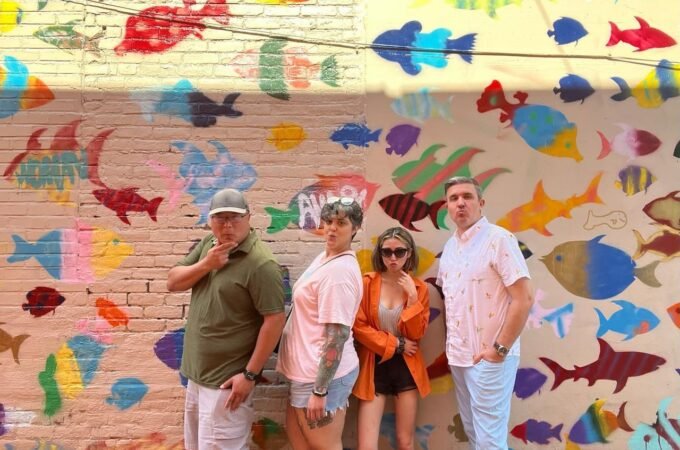 A group of individuals posing in front of a vibrant mural featuring many colorful fish silhouettes.