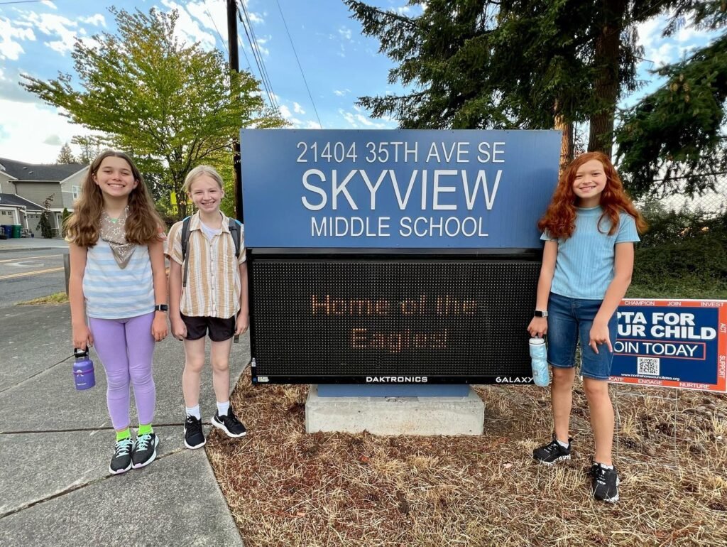 Young teenagers smiling in front of the Skyview Middle School sign on a sunny day.