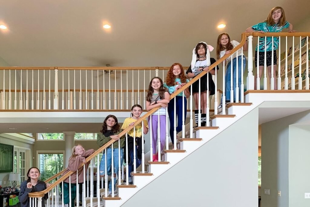 A large group poses on a wide wooden staircase inside a modern home.