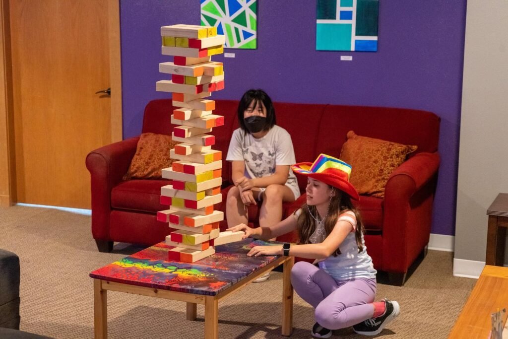Children playing with a large tower of colorful wooden blocks in a cozy living room.