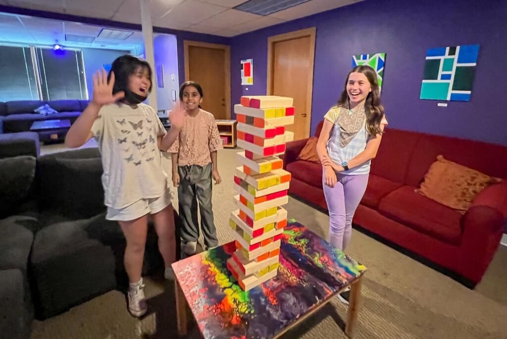 Three people playing a game of Jenga in a room with purple walls and red couches.