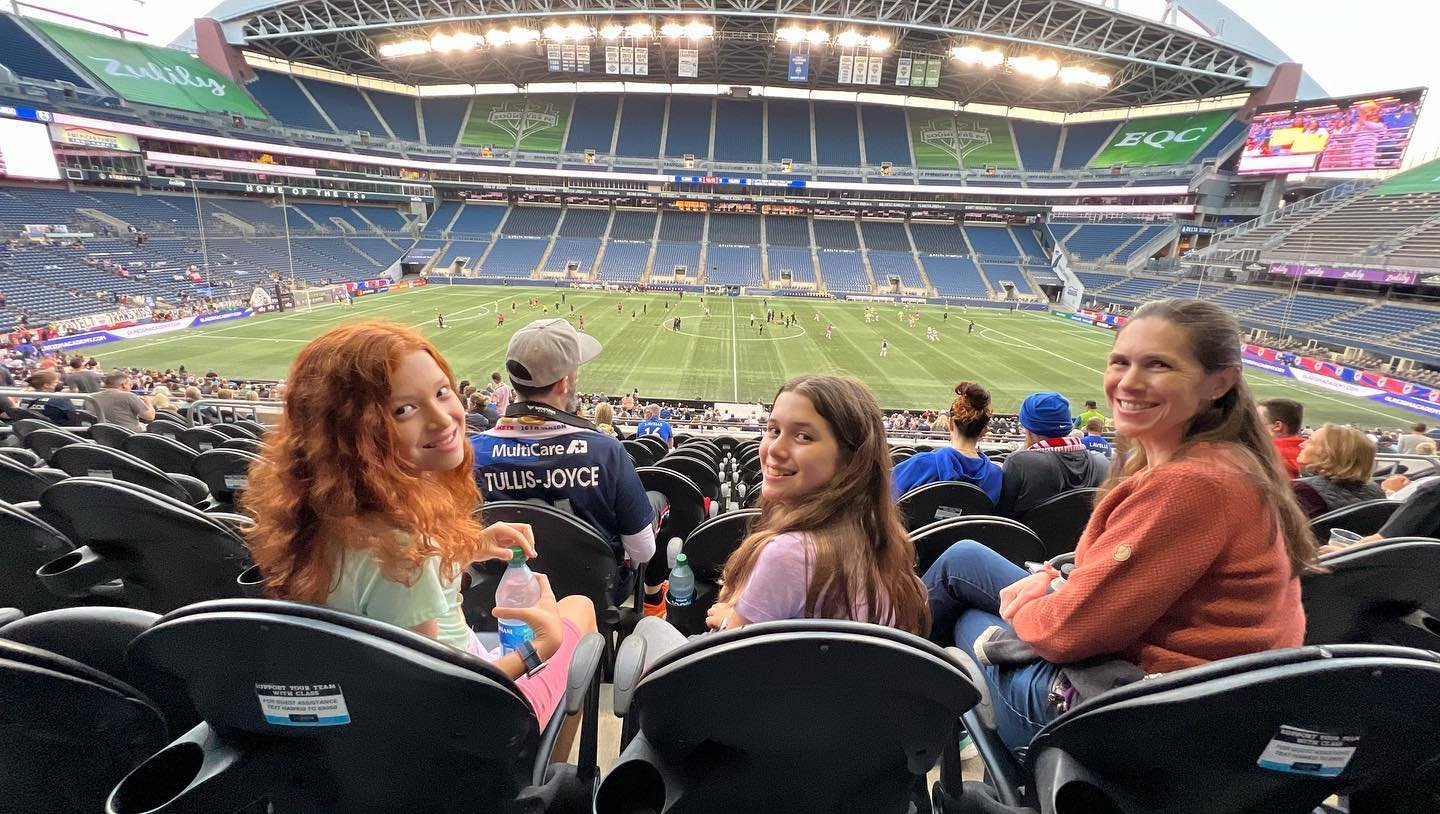 Friends and family enjoy a shared moment in the stands of a large outdoor stadium during a game.