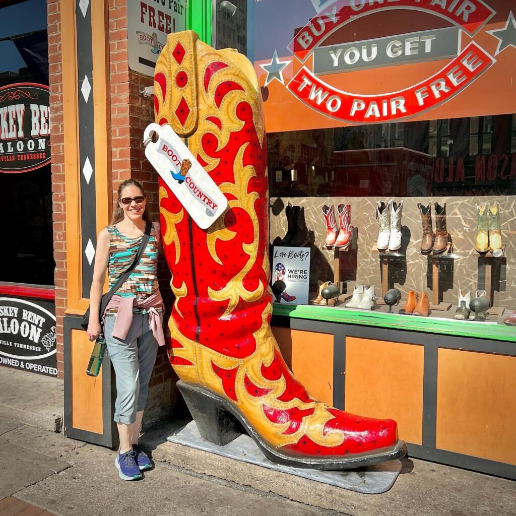 A person poses next to a giant red and yellow cowboy boot sculpture outside a storefront in the Pacific Northwest.