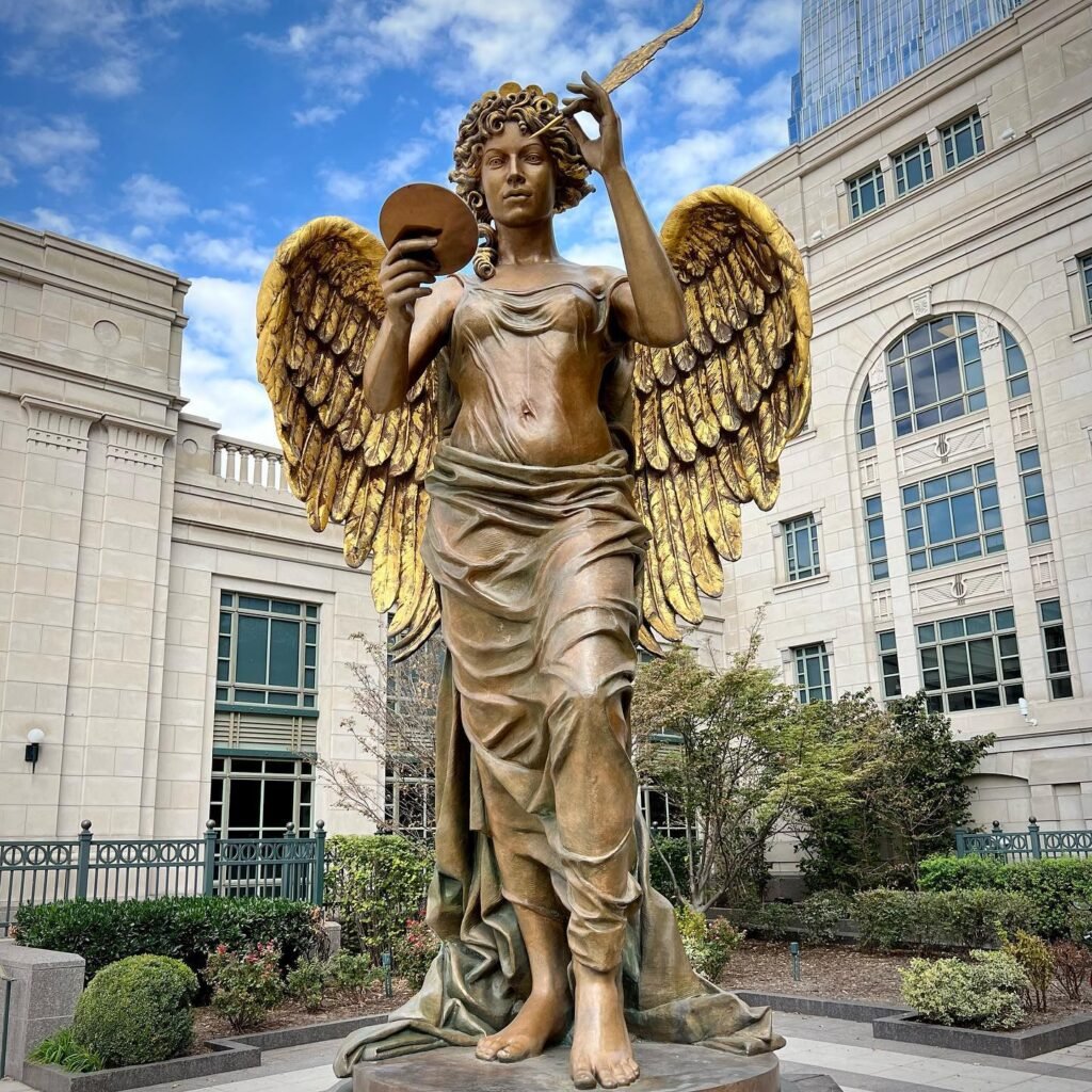 A golden winged statue holding a mirror and torch stands in an elegant courtyard with manicured gardens and classical architecture.