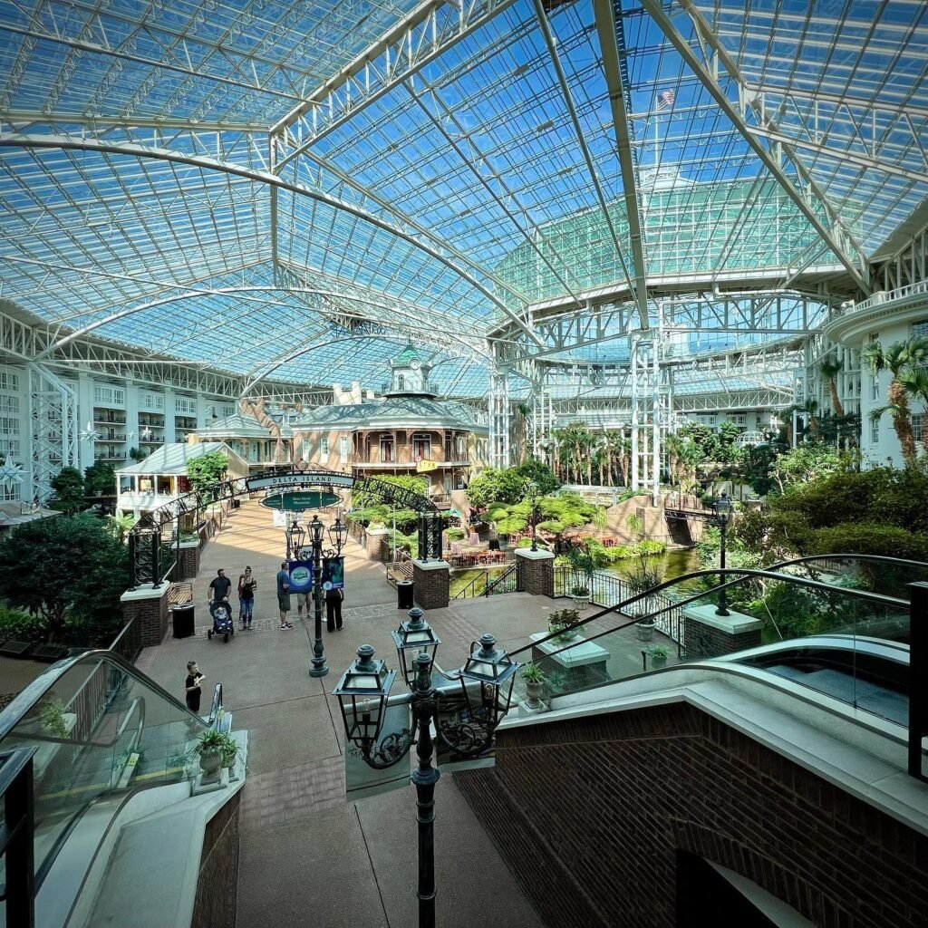 A spacious indoor conservatory with a glass ceiling and tropical plants.