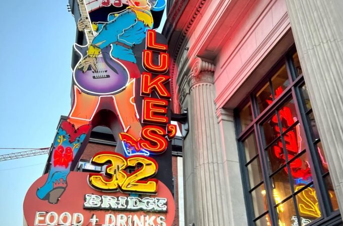 Vibrant neon sign for Luke's 32 adorning the exterior of the historic Paragon Building in Seattle. A colorful electric guitar icon highlights the restaurant's musical performance theme.