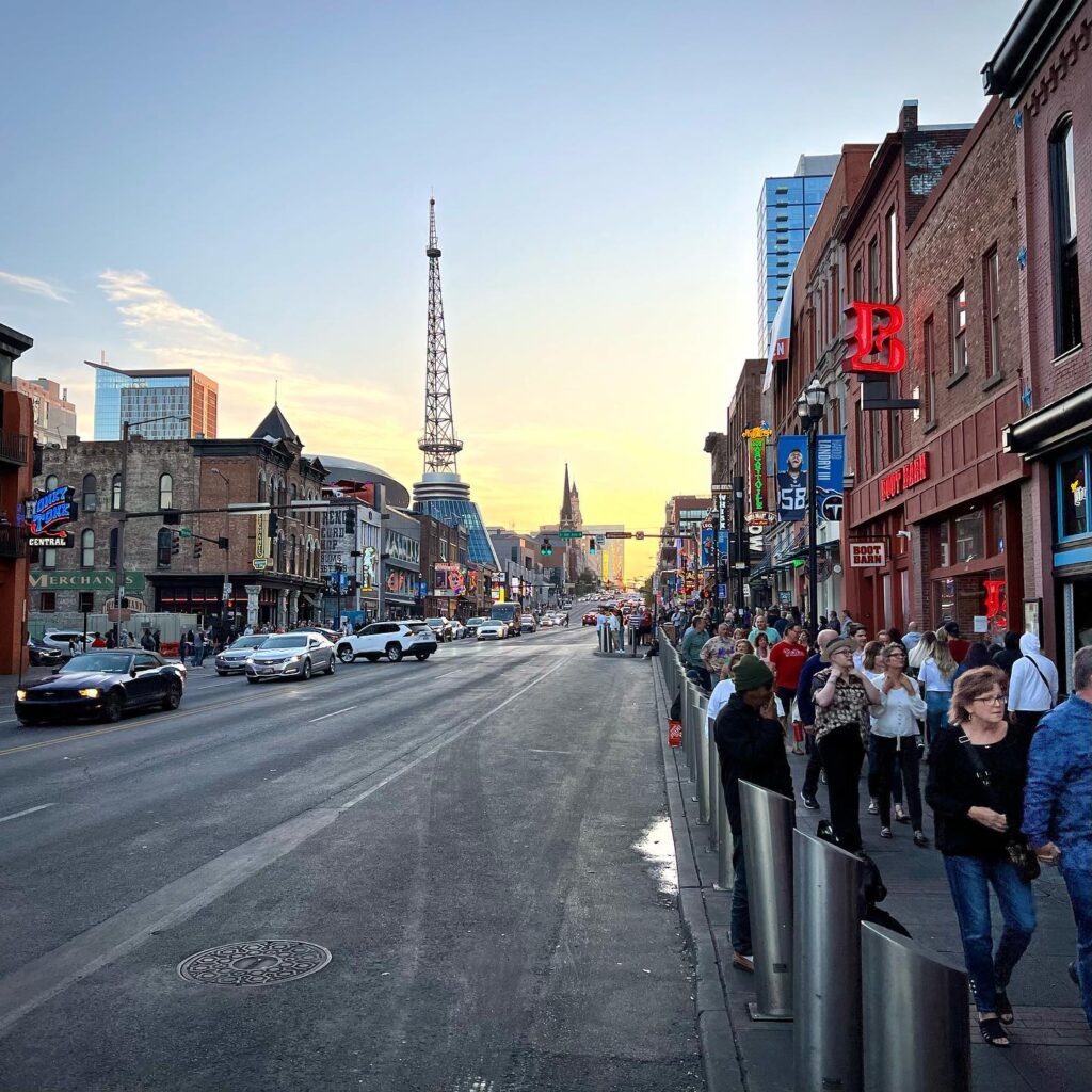 A busy city street in Vancouver featuring historic brick buildings and the Harbour Centre tower against the evening sky.