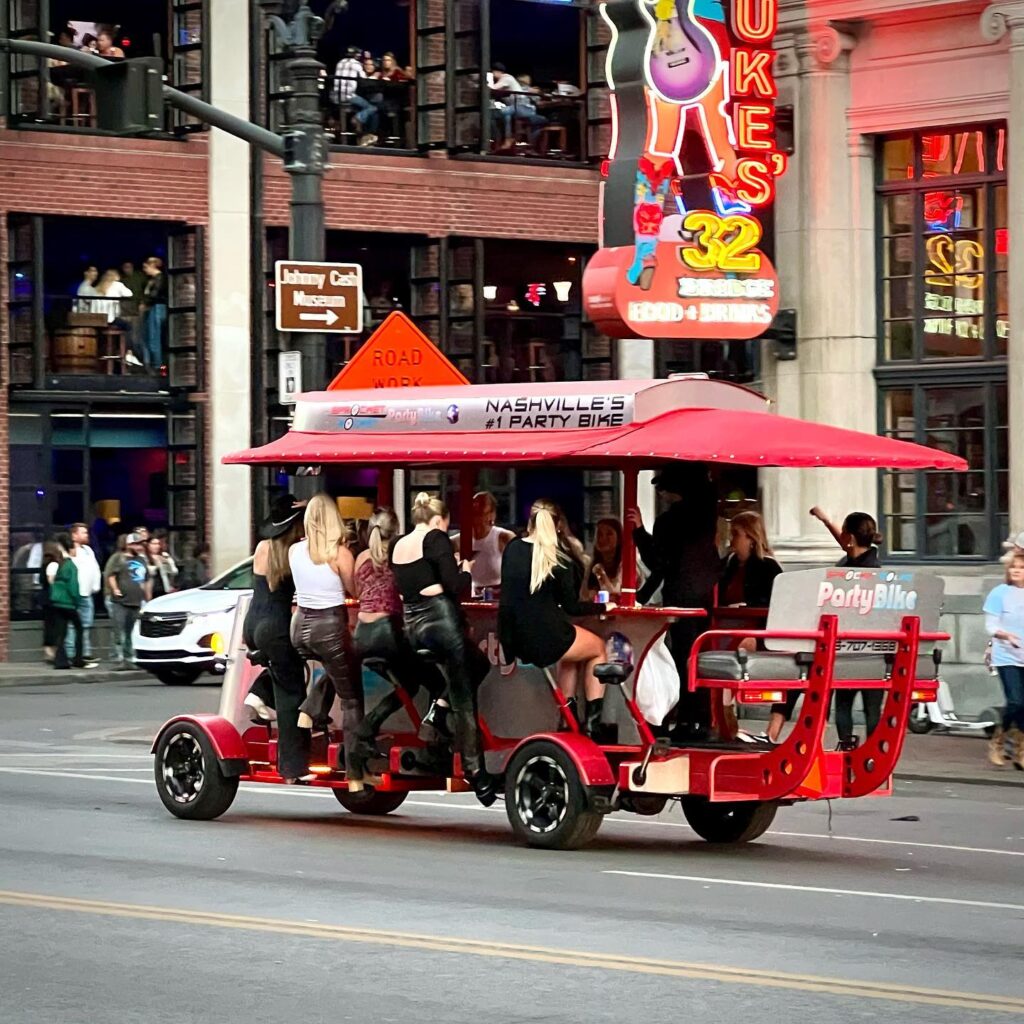 Red multi-seater party bike on downtown Nashville street with neon Horseshoe Tavern signage in background