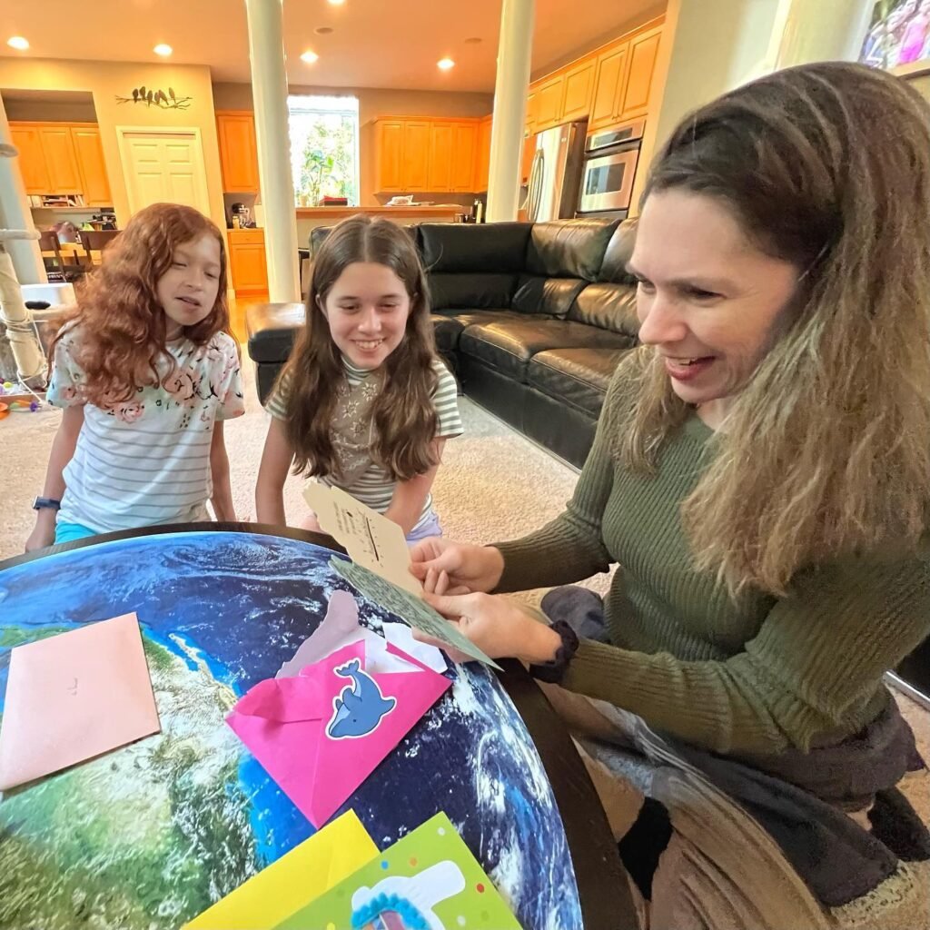 An adult and two children are gathered around a large globe, exploring geographical information together in a home living space.
