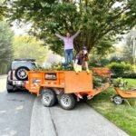 Stampede Pass Two people stand on top of a large orange trailer filled with green tree branches.