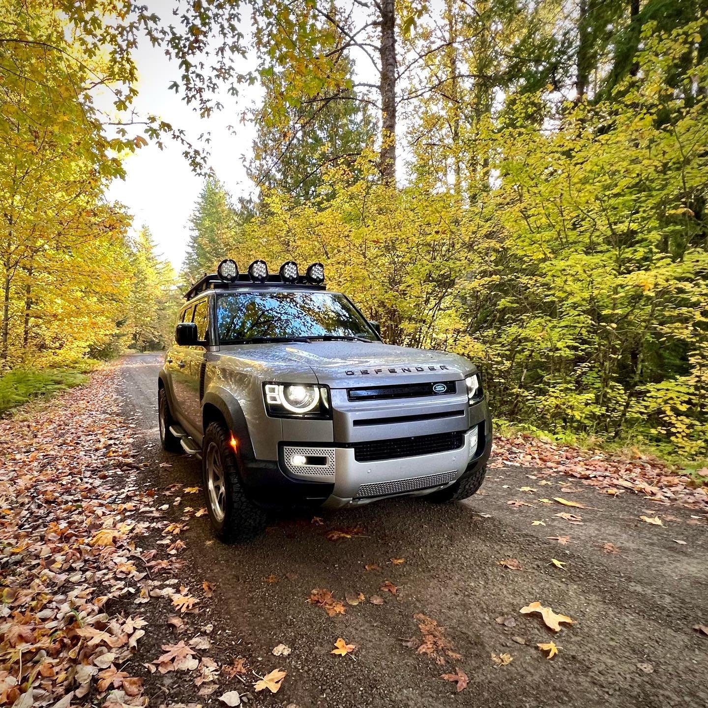 Stampede Pass A silver SUV with a rooftop light bar parked on a forest road surrounded by golden and green autumn trees.