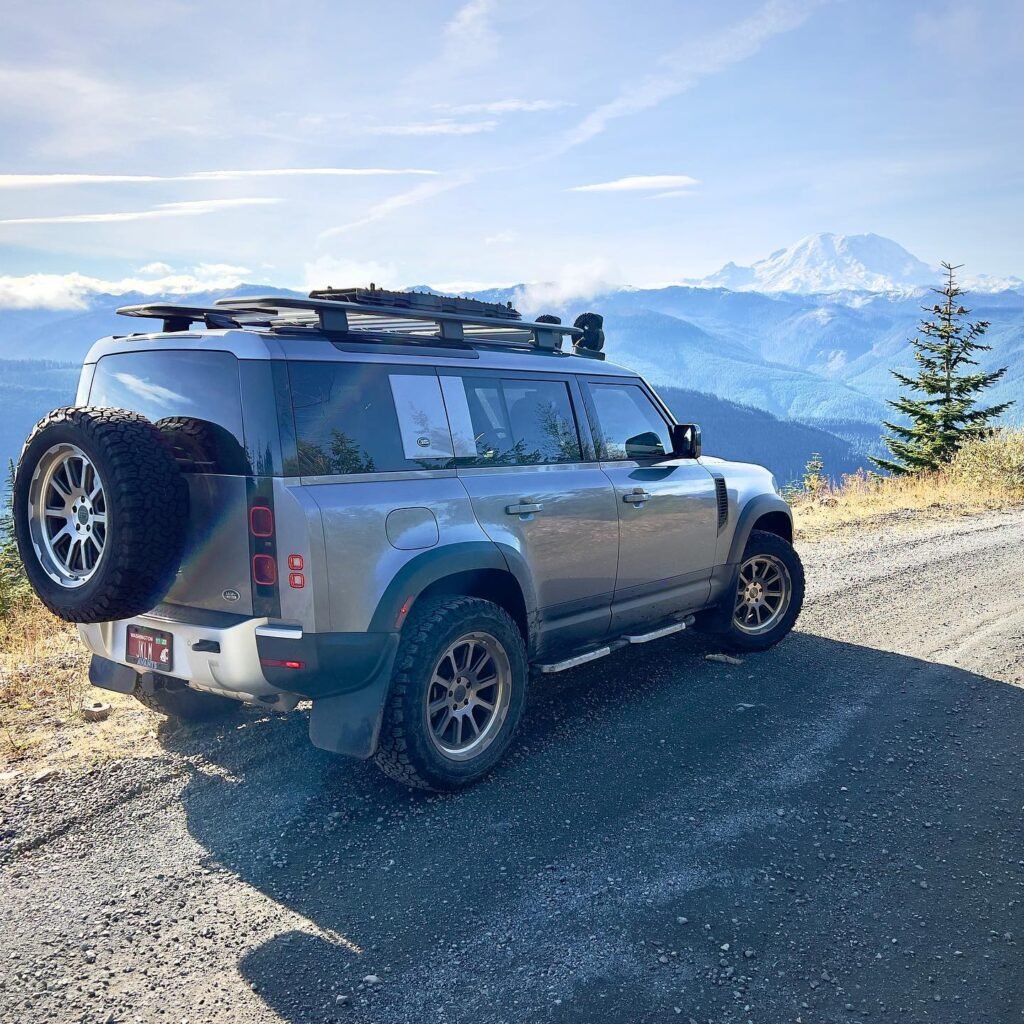 A silver SUV with a roof rack and mounted surfboards is parked on a mountain overlook.