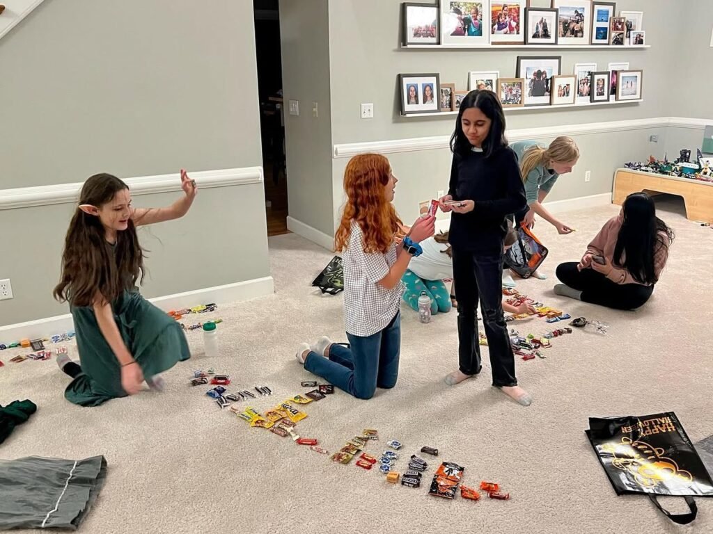 A group of girls play a board game on the living room floor surrounded by scattered pieces.