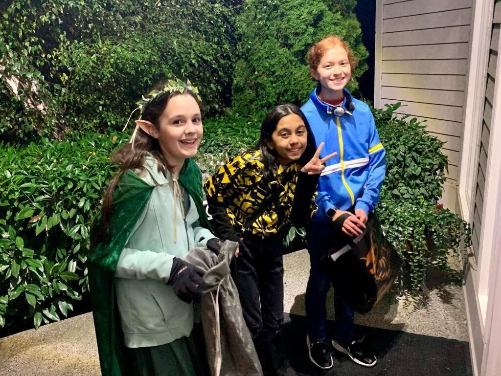 Three people in costumes posing outdoors, one dressed as an elf with a green cape and crown.