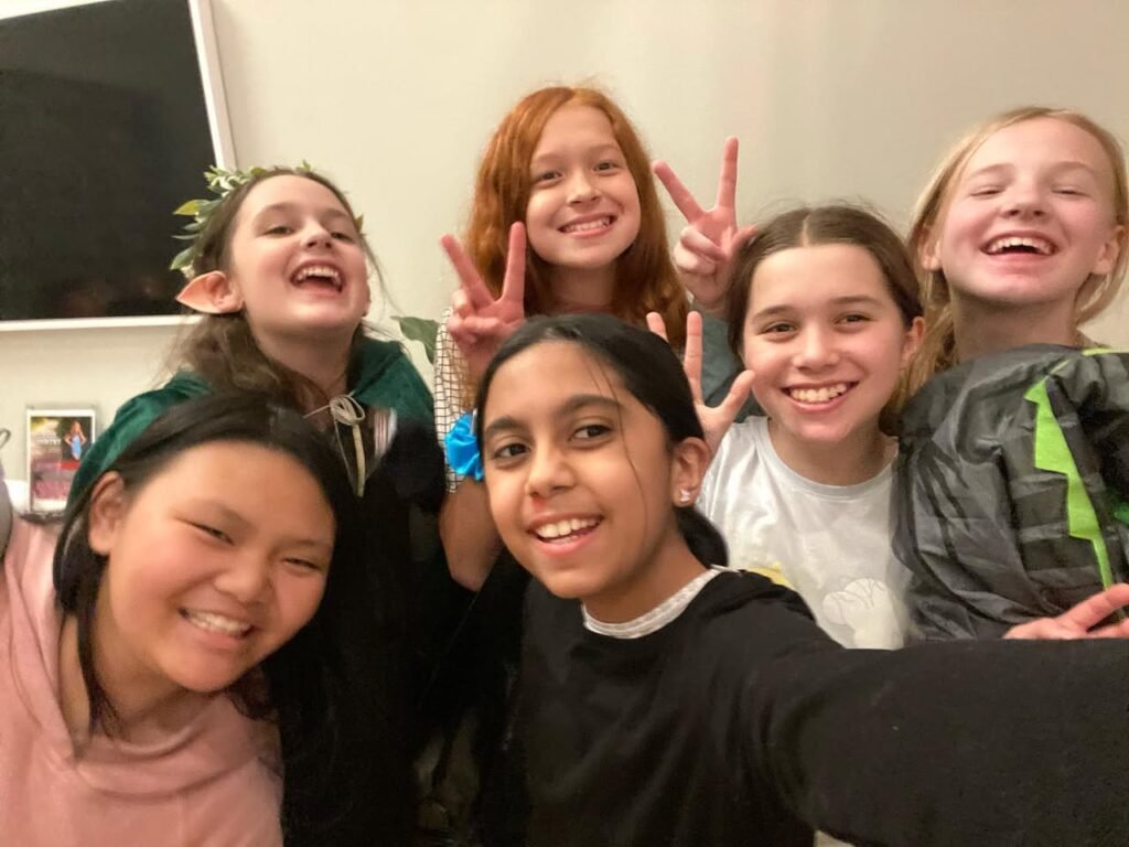 A group of people taking a selfie with smiles and peace signs indoors.