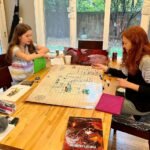 A fun family game night playing Settlers of Catan with a beautiful view of the backyard and a fountain outside the glass doors.