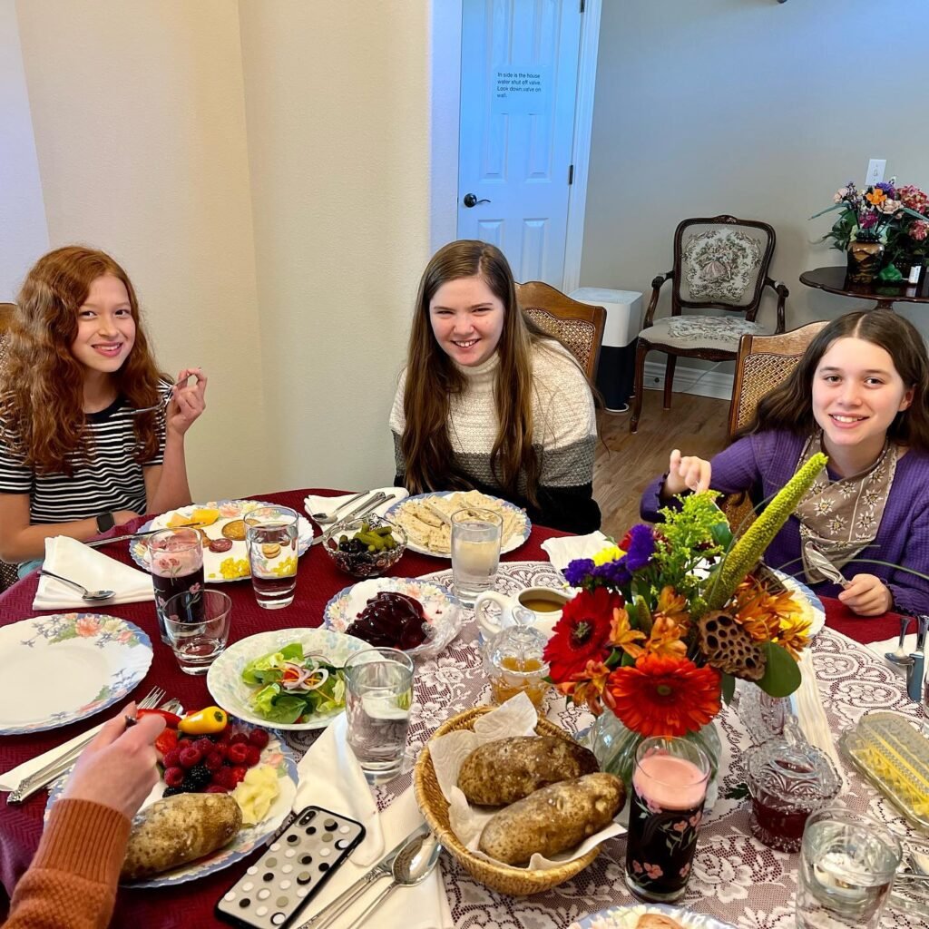 Female relatives enjoy a Thanksgiving dinner on a festive red table decorated with colorful flowers and grilled potatoes.