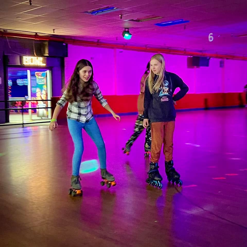 Two people on roller skates at an indoor rink with purple ambient lighting.