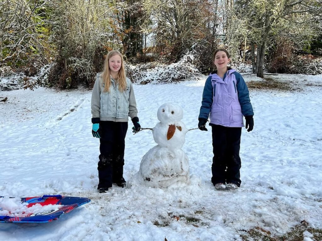 Two people enjoy a snowy day with a snowman and a sled.