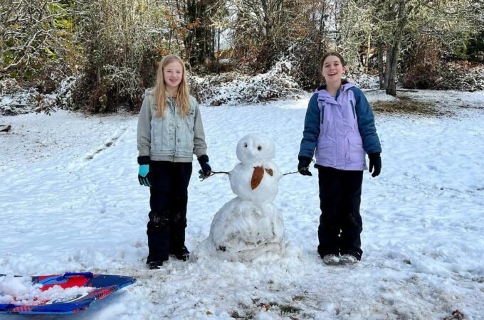 Two people enjoy a snowy day with a snowman and a sled.