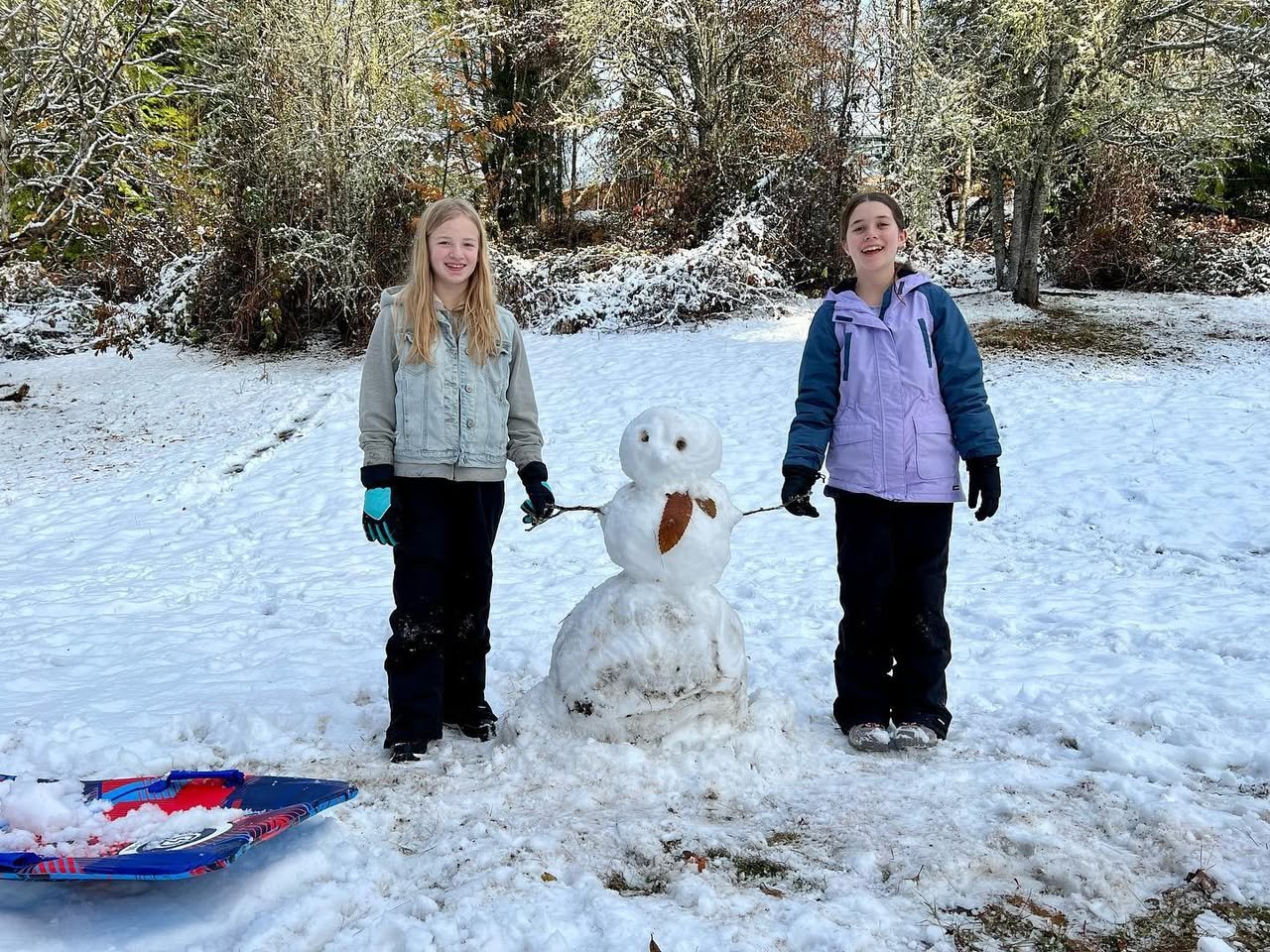 Two people enjoy a snowy day with a snowman and a sled.