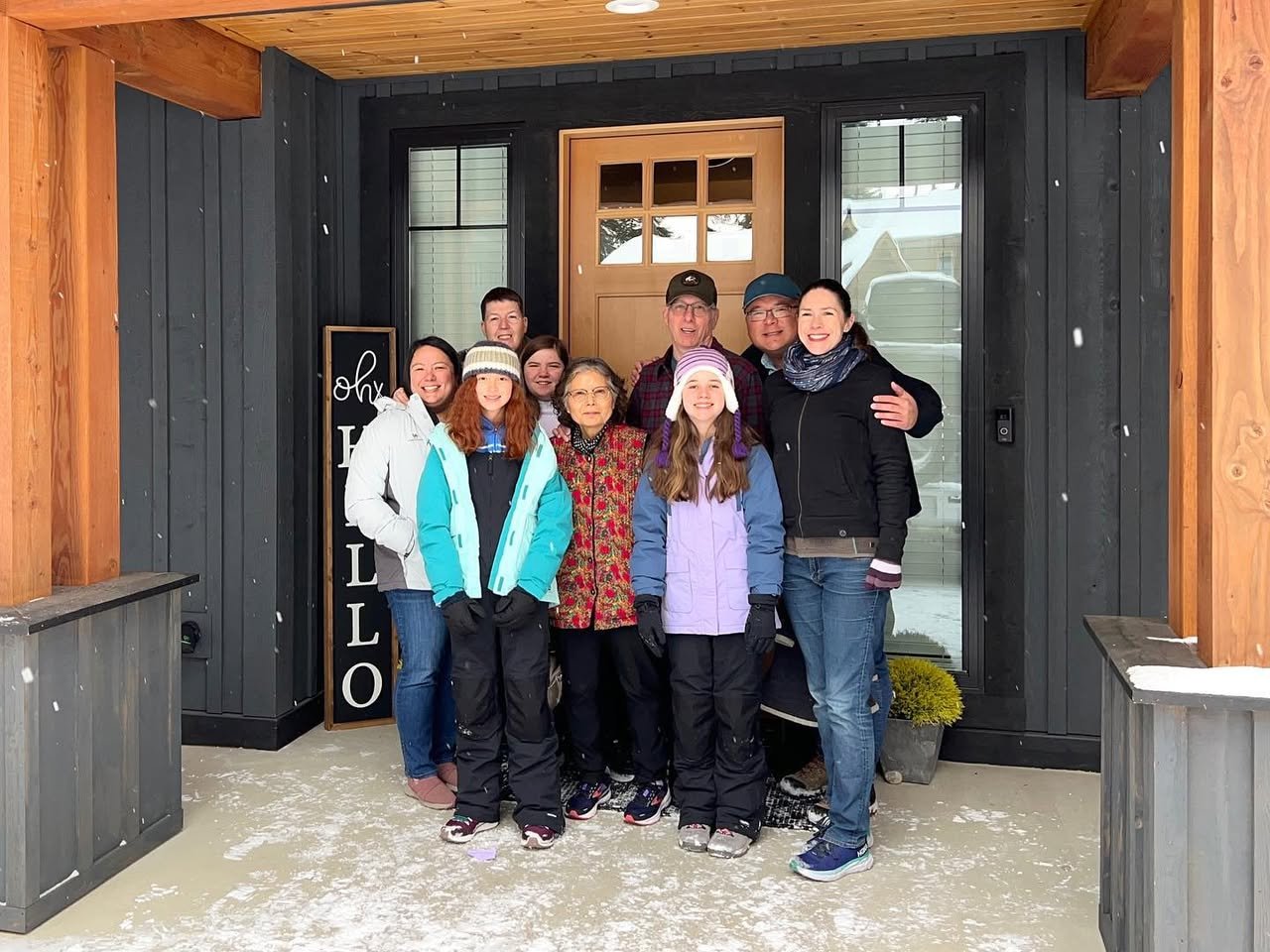 Suncadia Holidays A multi-generational family poses for a photo on the porch of a rustic lodge with dark wood siding. The entrance features heavy timber framing and a traditional wooden door with glass panels.