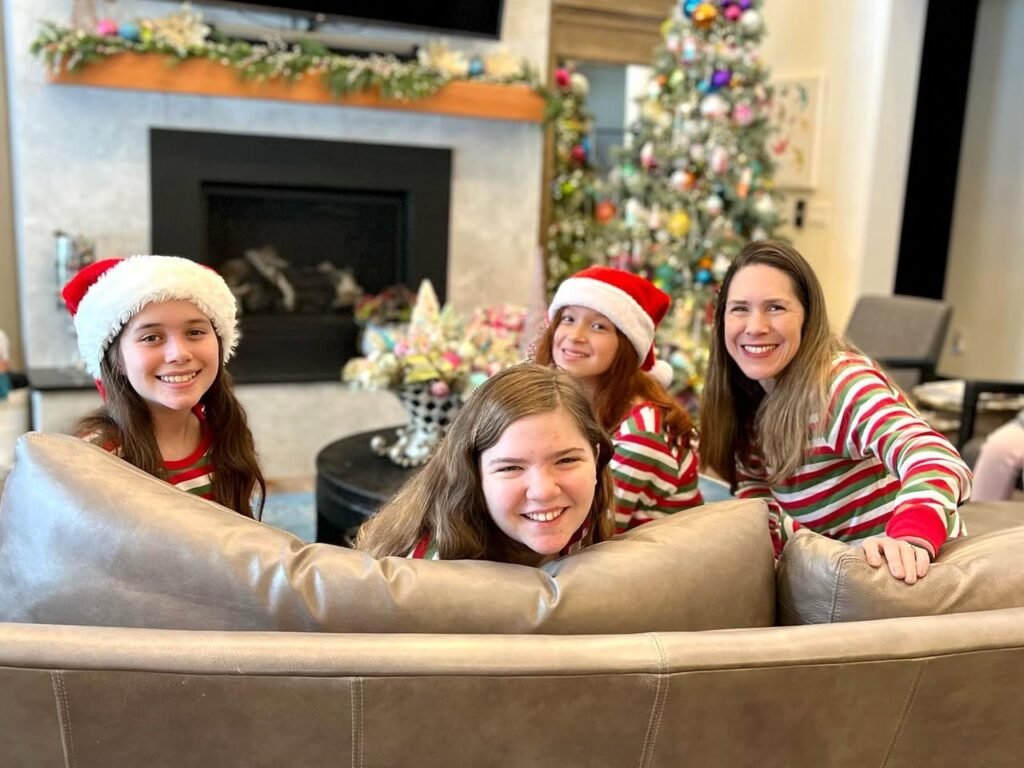 A family wearing festive Santa hats poses playfully on a couch in front of a decorated Christmas tree.
