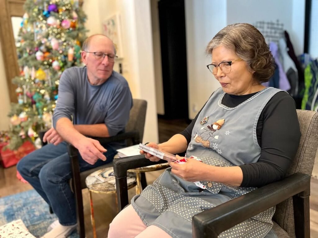 Two people sitting in chairs in front of a decorated Christmas tree. One person is holding a card game or tablet.