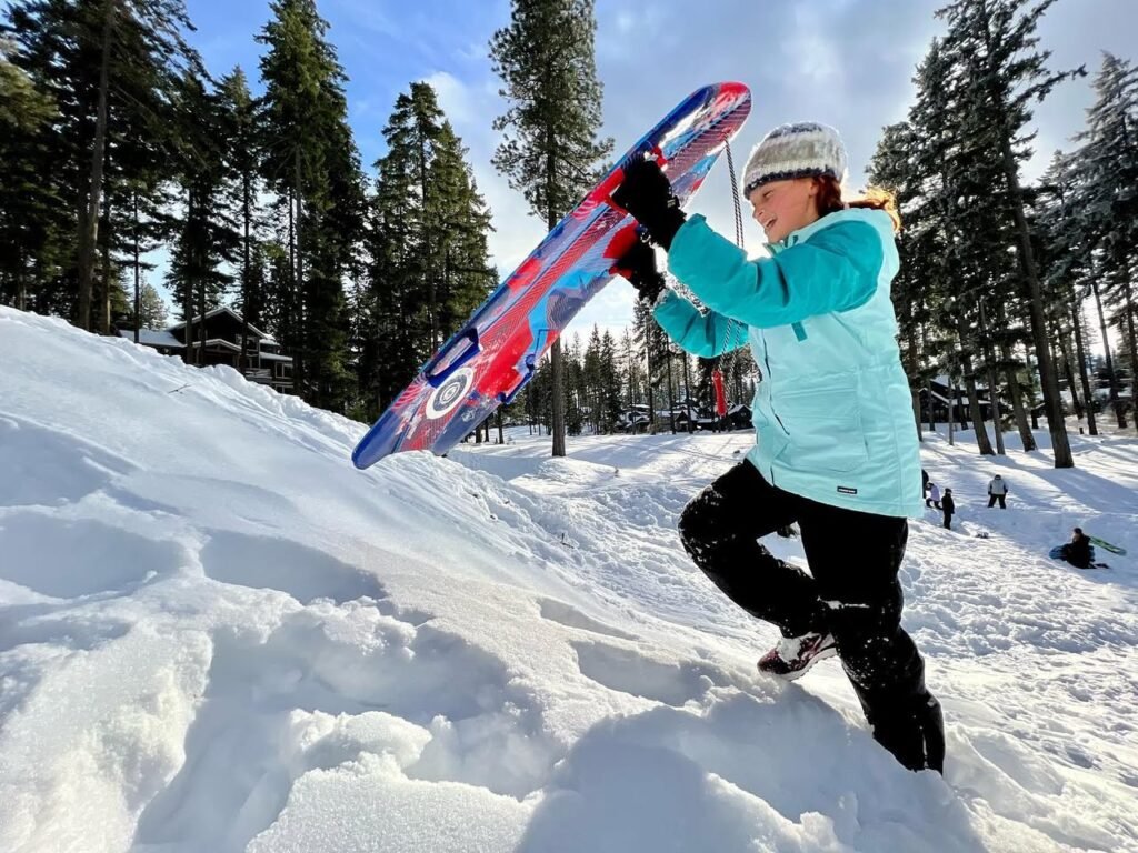 A person wearing a light blue jacket and black pants holds skis in a snowy landscape.
