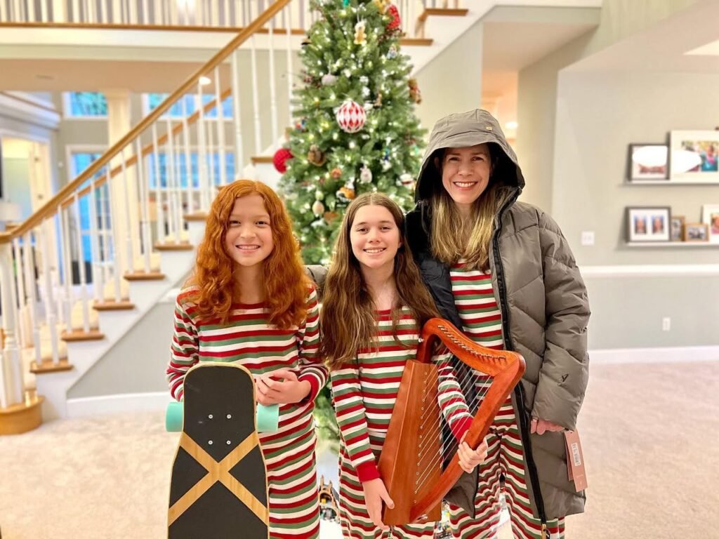 Family members in matching red and white striped pajamas holding a skateboard and harp in front of a Christmas tree.