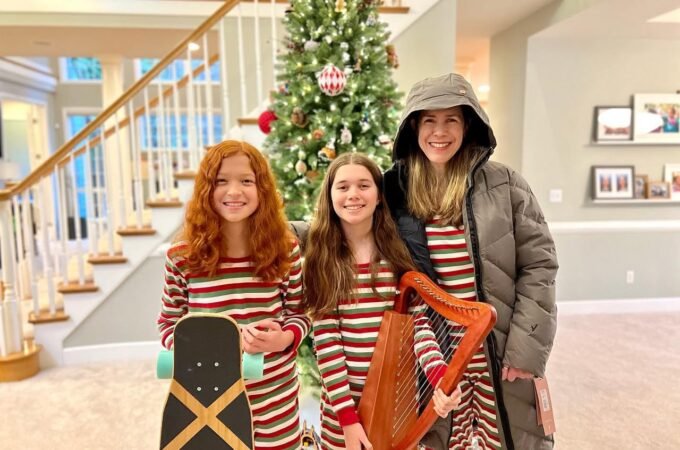 Family members in matching red and white striped pajamas holding a skateboard and harp in front of a Christmas tree.