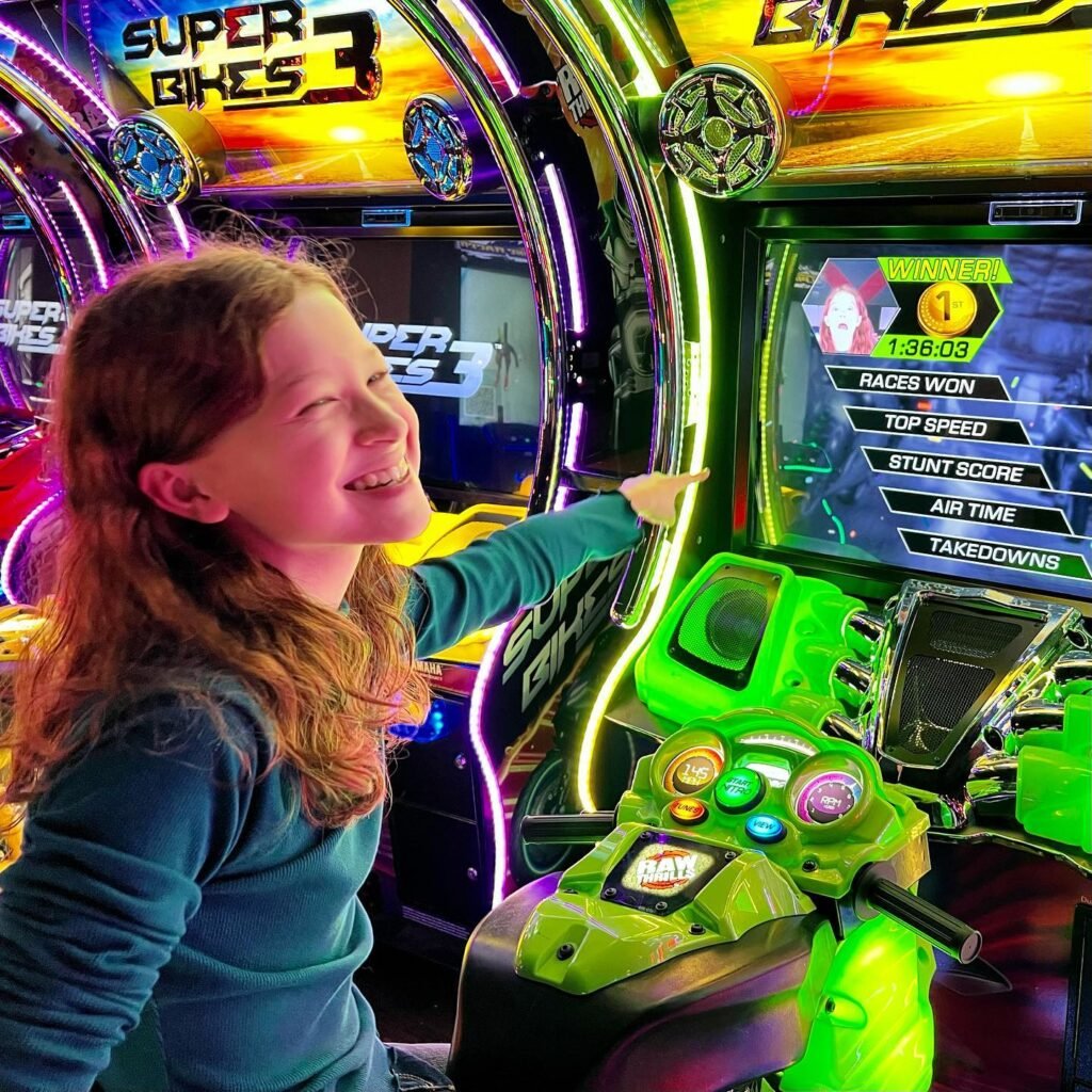 A child happily playing the Super Bikes 3 video game in a vibrant arcade setting.