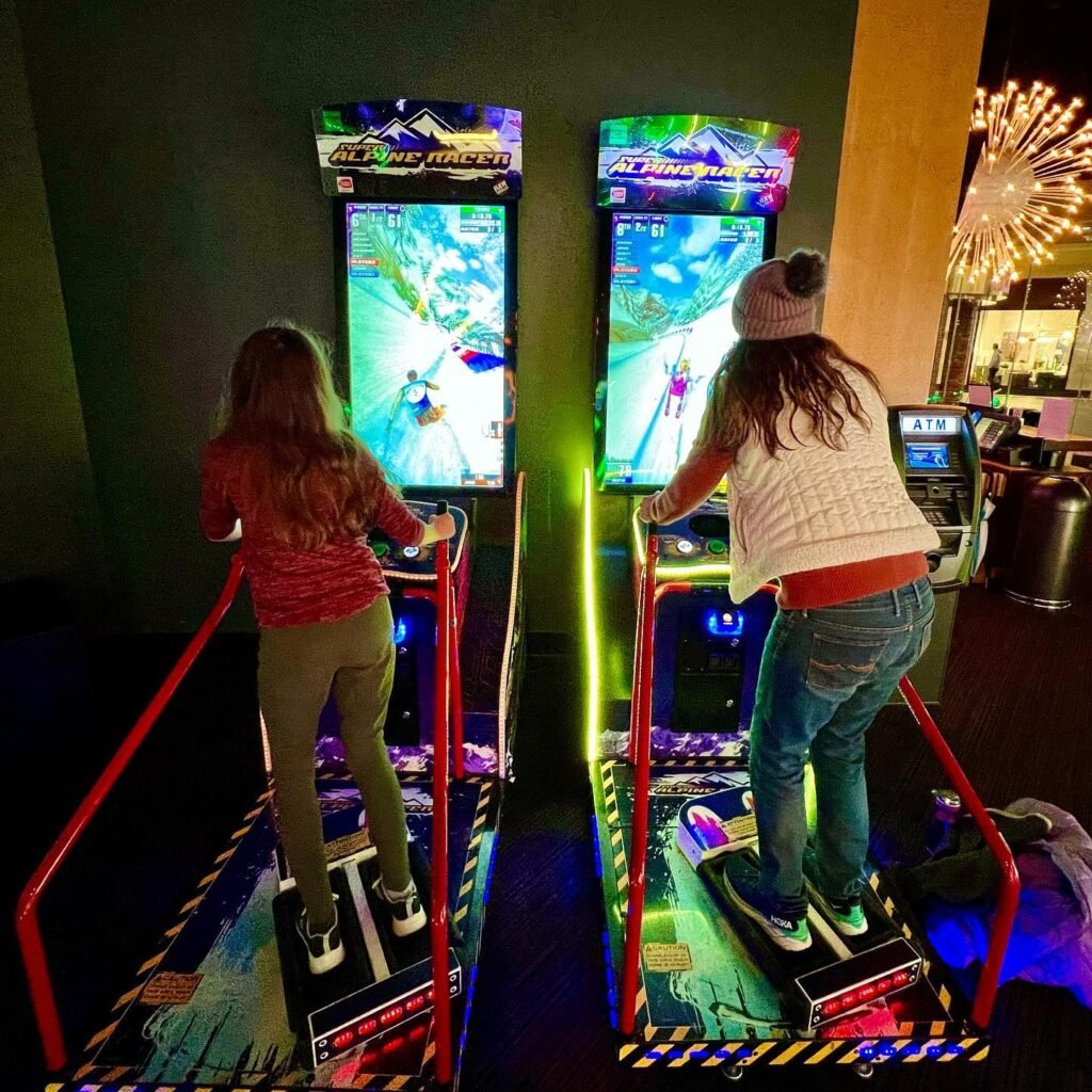 Two people enjoying the ski simulator game at an indoor amusement facility.