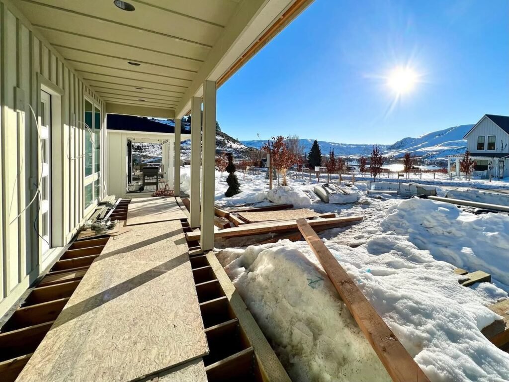 A striped porch deck under construction with a snowy yard and a sunny sky. The porch shows exposed wood frames and a clear view of the landscape.