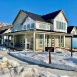A charming mountain chalet with snow covering the ground and surrounding landscape under a clear blue sky.