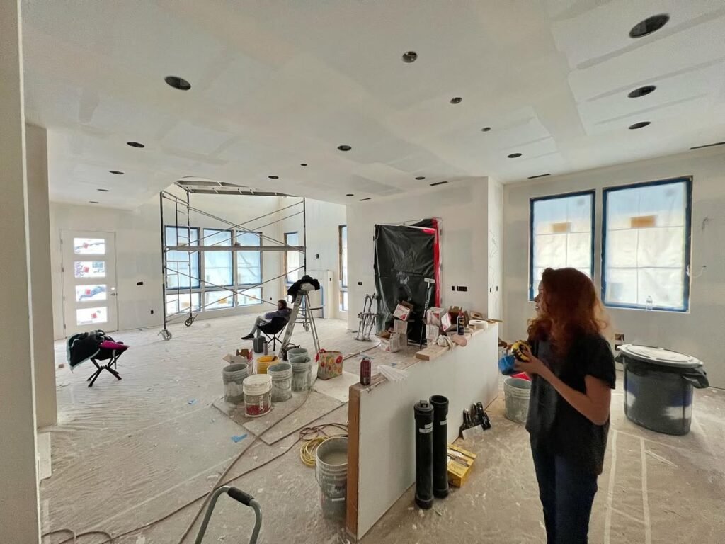 A living room undergoing renovation with new recessed ceiling lights and a protective plastic floor covering.