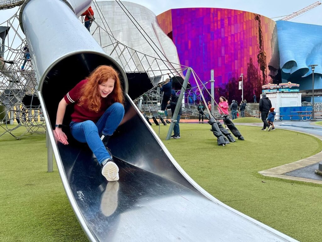 Sliding on a metal tube at the Olympic Park Tower playground in London during a family travel adventure.