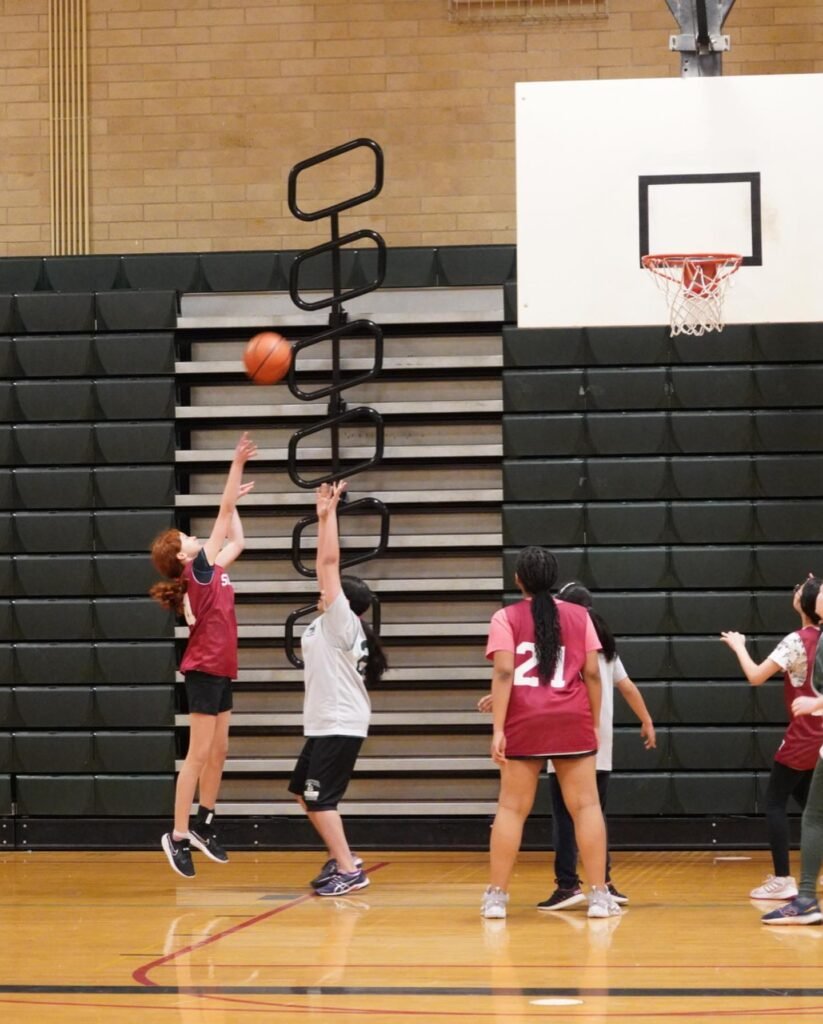 A junior high school girls basketball team practicing in an indoor gym.